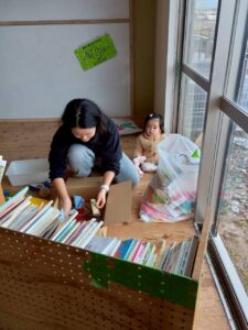 座って本端を片づけるスタッフの横で窓の外を見つめる0歳児