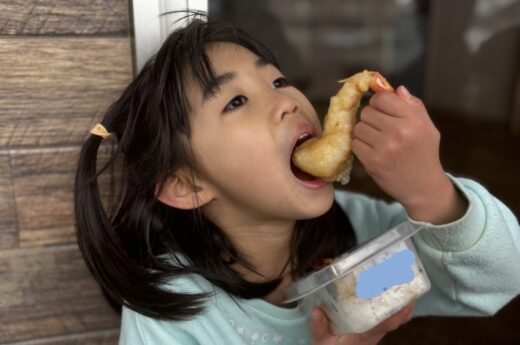 お弁当箱を片手にえび天をほおばる女の子